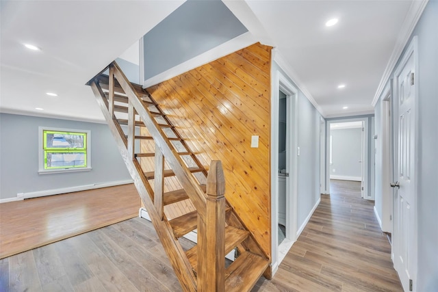 stairs featuring hardwood / wood-style flooring, crown molding, baseboard heating, and wood walls