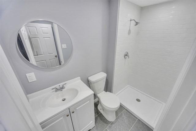 bathroom with tile patterned flooring, vanity, a tile shower, and toilet