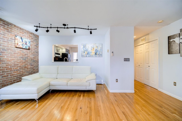 unfurnished living room featuring brick wall, rail lighting, and light hardwood / wood-style flooring