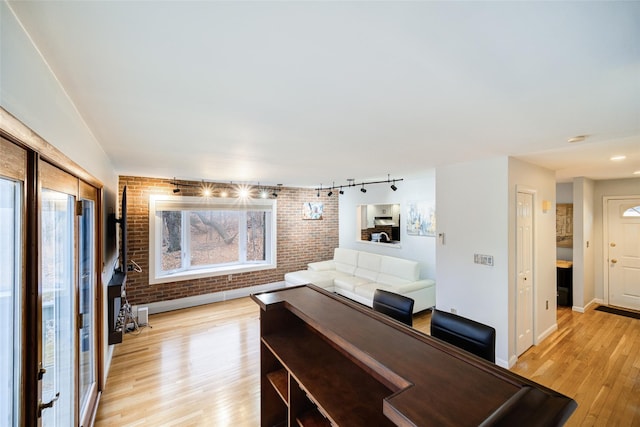 interior space with track lighting, light hardwood / wood-style floors, and brick wall