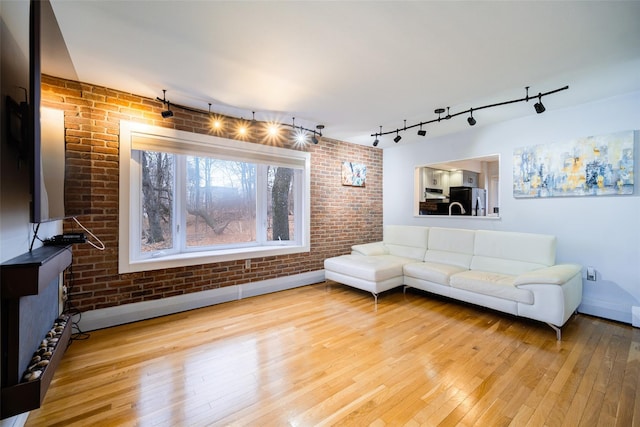 living room with brick wall, rail lighting, and light wood-type flooring