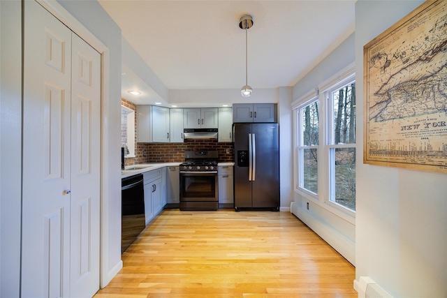 kitchen featuring sink, appliances with stainless steel finishes, tasteful backsplash, decorative light fixtures, and light wood-type flooring