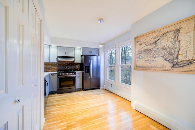 kitchen featuring appliances with stainless steel finishes, decorative light fixtures, decorative backsplash, baseboard heating, and light hardwood / wood-style floors