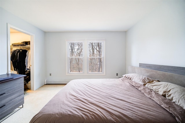 bedroom featuring a walk in closet, light colored carpet, a closet, and a baseboard heating unit