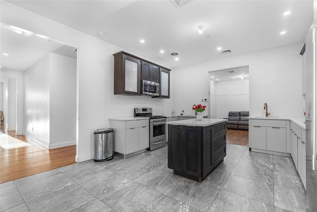 kitchen with appliances with stainless steel finishes, sink, a center island, kitchen peninsula, and dark brown cabinets