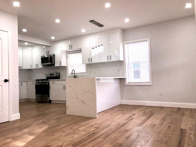 kitchen featuring stainless steel appliances, pendant lighting, white cabinets, and light hardwood / wood-style flooring