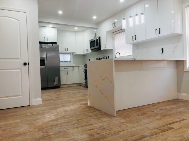 kitchen with white cabinets, hanging light fixtures, kitchen peninsula, stainless steel appliances, and light hardwood / wood-style flooring