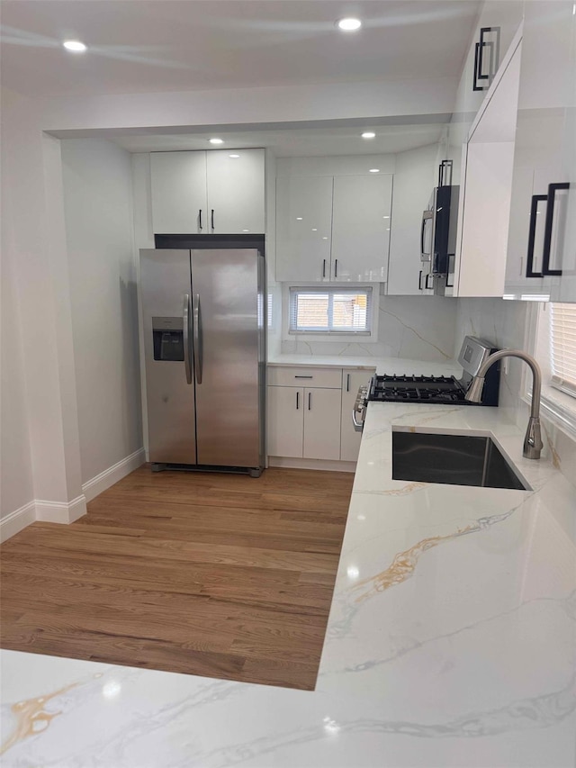 kitchen with sink, white cabinetry, light stone counters, light wood-type flooring, and stainless steel appliances