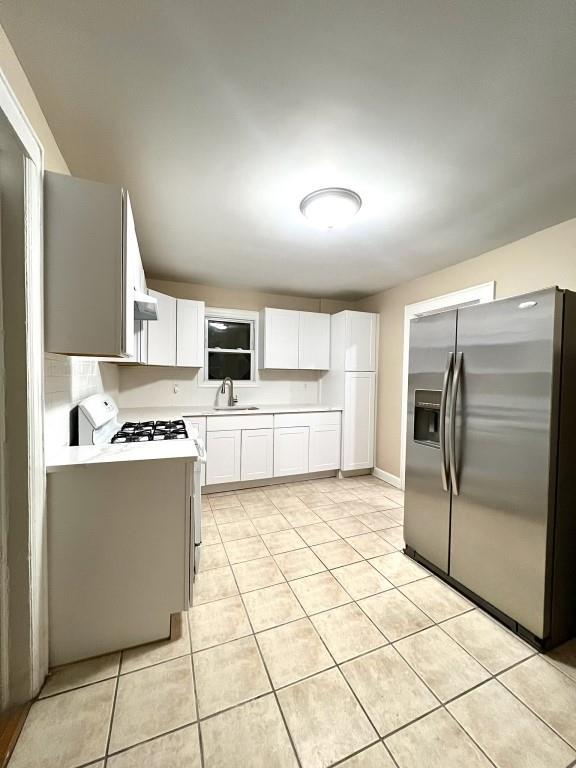 kitchen with sink, gas range gas stove, stainless steel refrigerator with ice dispenser, white cabinets, and light tile patterned flooring