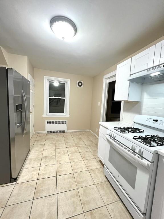 kitchen with white gas stove, white cabinetry, stainless steel fridge with ice dispenser, light tile patterned floors, and radiator heating unit