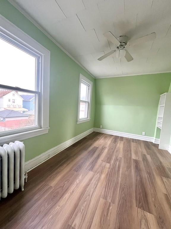 empty room featuring crown molding, radiator, hardwood / wood-style floors, and ceiling fan