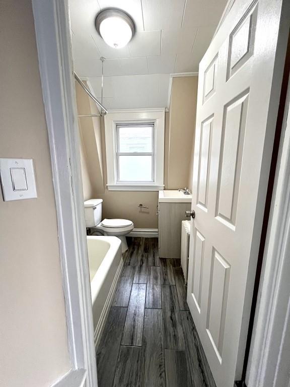 bathroom with wood-type flooring, a washtub, vanity, and toilet