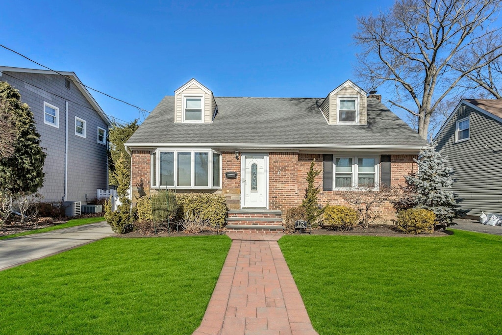 cape cod house featuring central AC and a front lawn