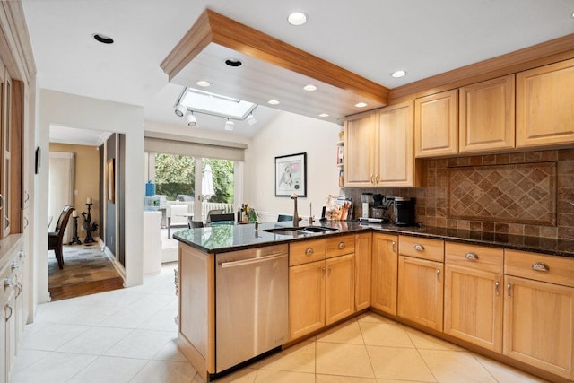 kitchen with a skylight, stainless steel dishwasher, dark stone counters, and kitchen peninsula