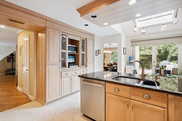 kitchen with light brown cabinetry, a skylight, sink, dark stone counters, and stainless steel appliances