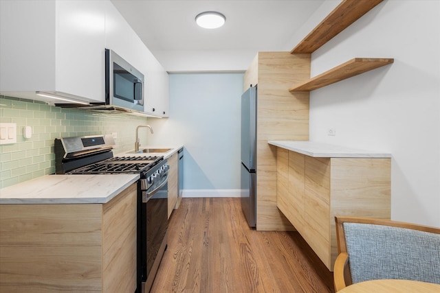 kitchen with sink, white cabinetry, stainless steel appliances, light hardwood / wood-style floors, and backsplash