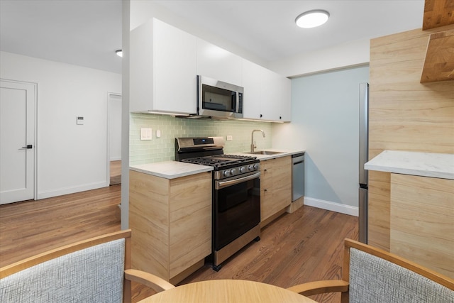 kitchen with sink, white cabinetry, wood-type flooring, stainless steel appliances, and decorative backsplash