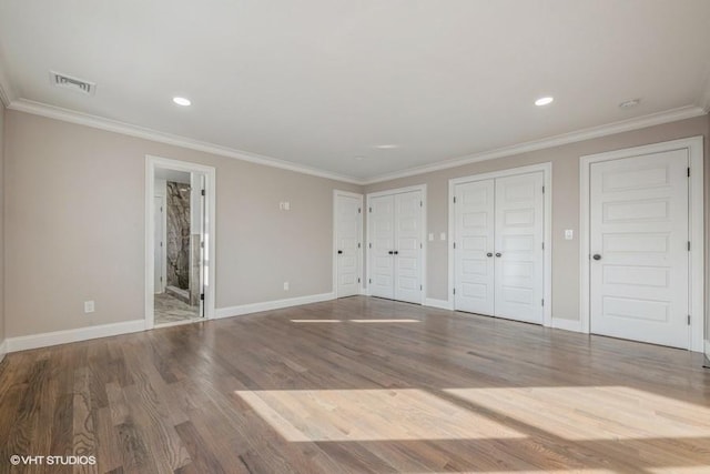 unfurnished bedroom featuring crown molding, two closets, wood-type flooring, and connected bathroom