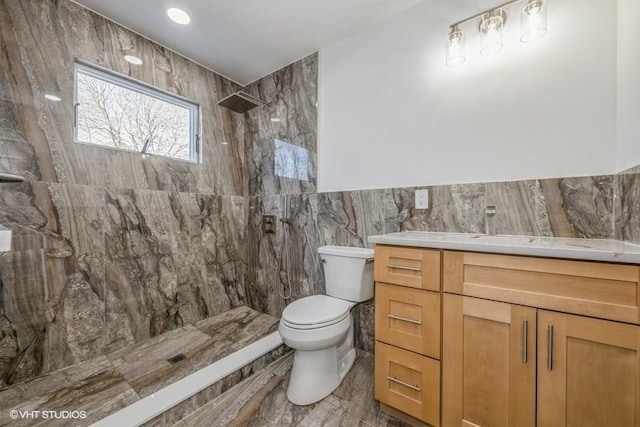 bathroom featuring tiled shower, vanity, toilet, and tile walls