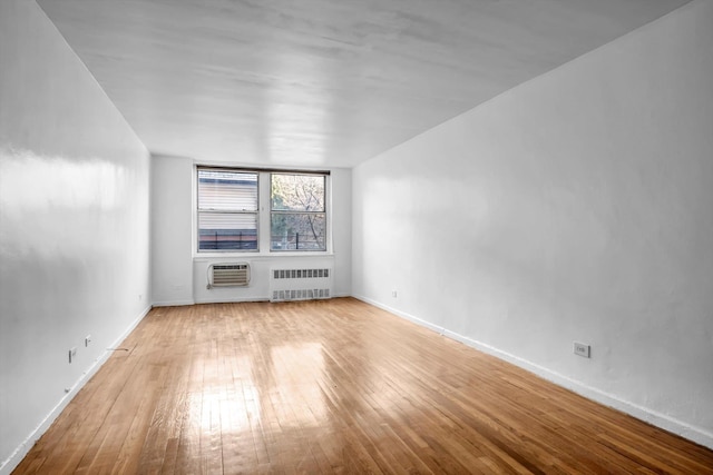 spare room with radiator heating unit, a wall mounted AC, and light wood-type flooring