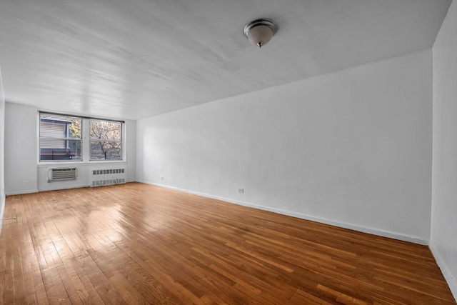 unfurnished living room with hardwood / wood-style floors, a wall mounted air conditioner, and radiator heating unit