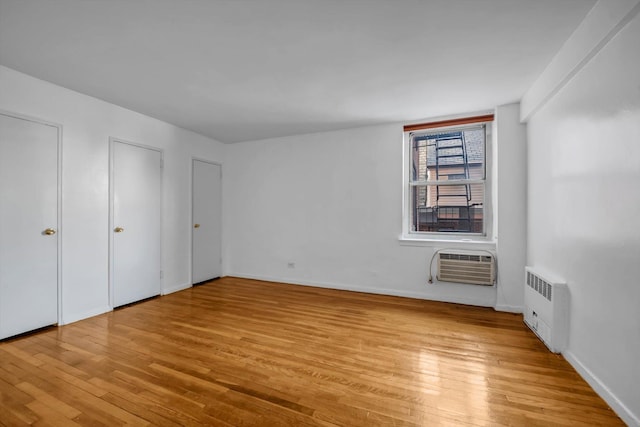 unfurnished bedroom with radiator, a wall unit AC, multiple closets, and light wood-type flooring