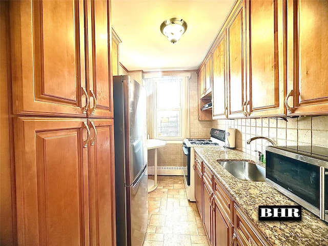 kitchen with a sink, stone tile flooring, brown cabinets, stainless steel appliances, and light stone counters