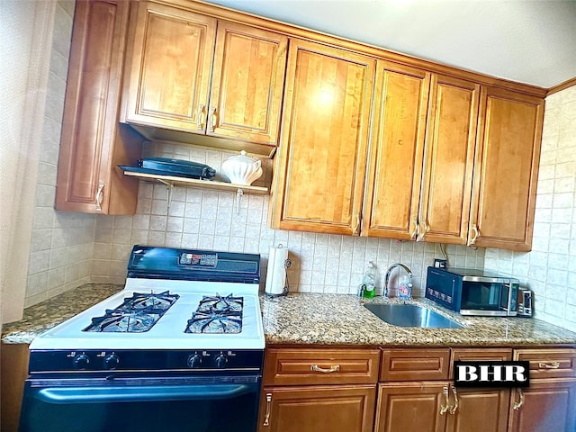 kitchen featuring tasteful backsplash, gas stove, light stone counters, brown cabinets, and a sink