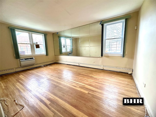 unfurnished room featuring a baseboard radiator, a healthy amount of sunlight, and hardwood / wood-style flooring