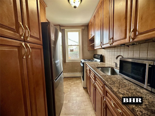 kitchen featuring stone tile floors, dark stone countertops, appliances with stainless steel finishes, a sink, and brown cabinets