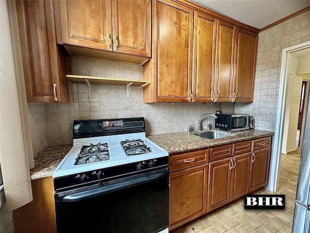kitchen with brown cabinetry, tasteful backsplash, gas range, stainless steel microwave, and a sink