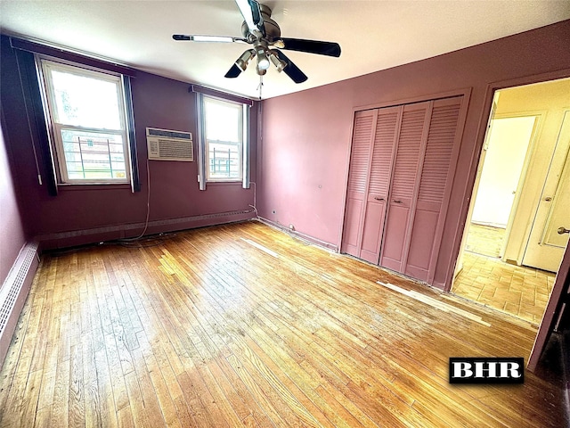 unfurnished bedroom featuring baseboard heating, a closet, a wall mounted air conditioner, a ceiling fan, and light wood finished floors
