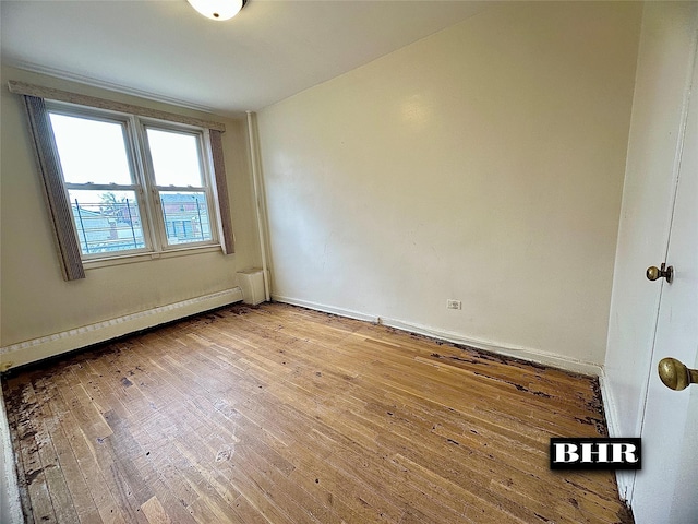 spare room featuring wood-type flooring, baseboards, and a baseboard heating unit