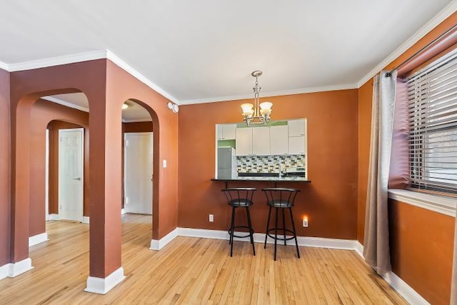 dining area featuring an inviting chandelier, sink, ornamental molding, and light wood-type flooring