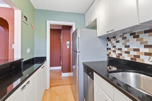 kitchen with sink, light wood-type flooring, stainless steel dishwasher, white cabinets, and backsplash