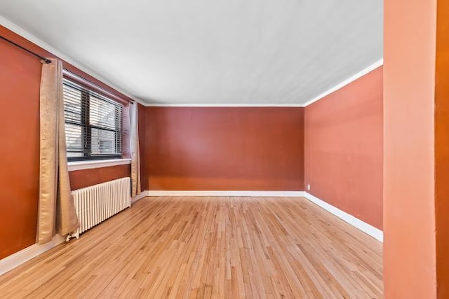 empty room featuring ornamental molding, radiator heating unit, and light wood-type flooring