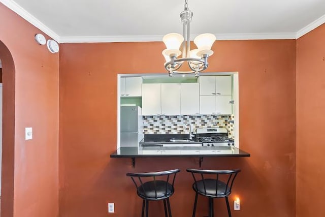 kitchen with a kitchen breakfast bar, pendant lighting, stainless steel appliances, decorative backsplash, and white cabinets