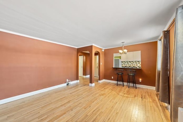 unfurnished living room with a notable chandelier, ornamental molding, and light wood-type flooring