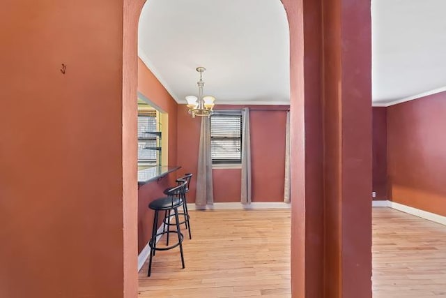 bar with pendant lighting, a notable chandelier, light hardwood / wood-style flooring, and ornamental molding