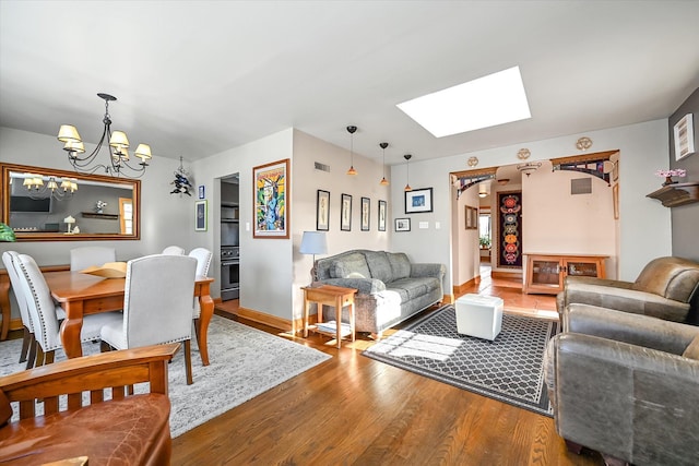 living room with hardwood / wood-style flooring, a skylight, and an inviting chandelier