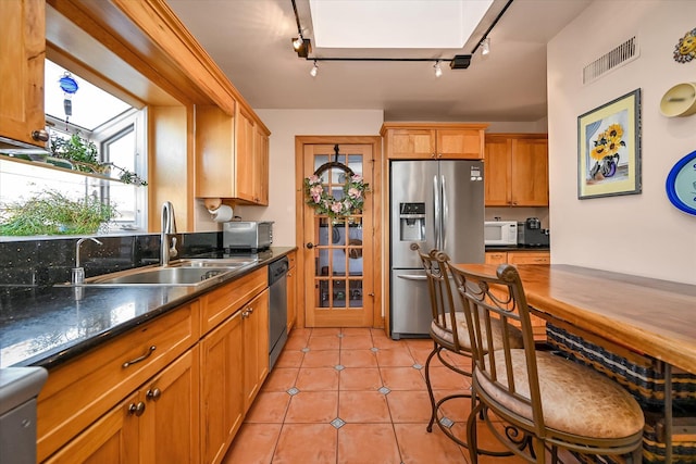 kitchen with light tile patterned flooring, rail lighting, sink, dark stone countertops, and stainless steel appliances