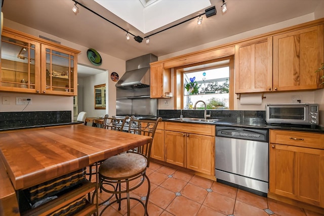 kitchen with sink, dark stone countertops, light tile patterned floors, stainless steel appliances, and wall chimney range hood