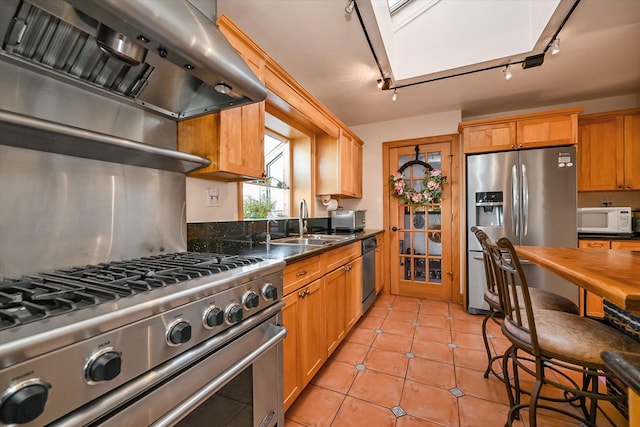 kitchen featuring appliances with stainless steel finishes, a skylight, range hood, sink, and light tile patterned floors