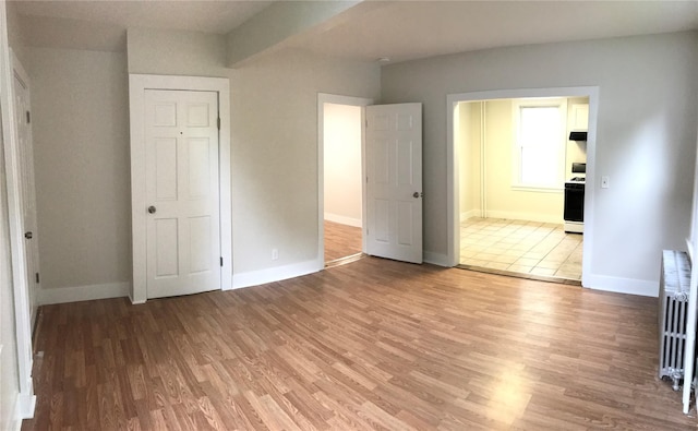 unfurnished bedroom featuring ensuite bathroom, wood-type flooring, radiator, and a closet