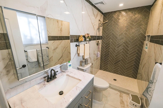 bathroom featuring tile walls, vanity, toilet, and a tile shower