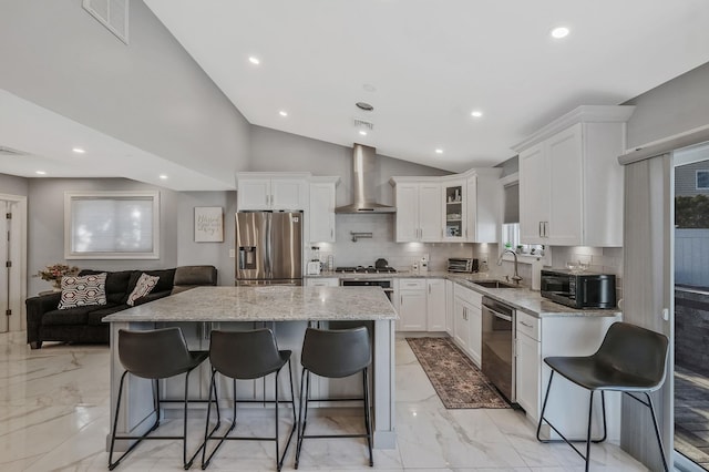 kitchen with a kitchen bar, sink, a kitchen island, stainless steel appliances, and wall chimney range hood