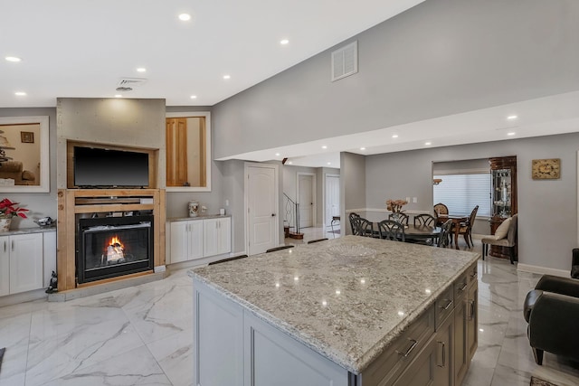 kitchen featuring light stone counters, a fireplace, a center island, and white cabinets