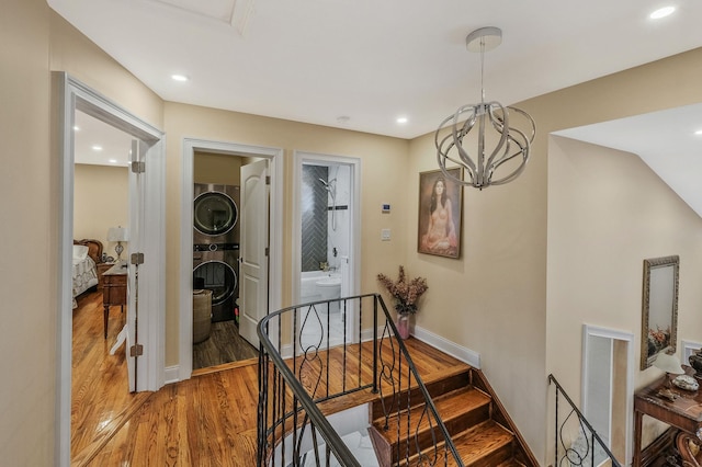 hall featuring hardwood / wood-style flooring, stacked washer / drying machine, and an inviting chandelier