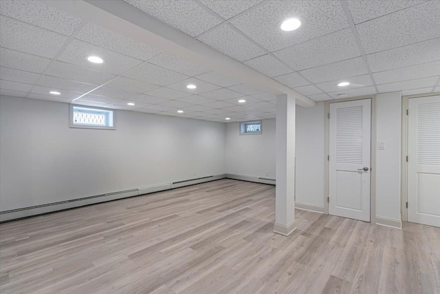 basement with light hardwood / wood-style flooring, baseboard heating, and a paneled ceiling