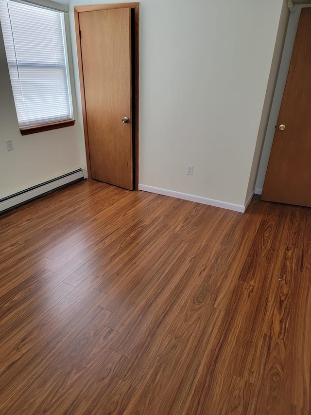 empty room featuring dark hardwood / wood-style flooring and a baseboard heating unit